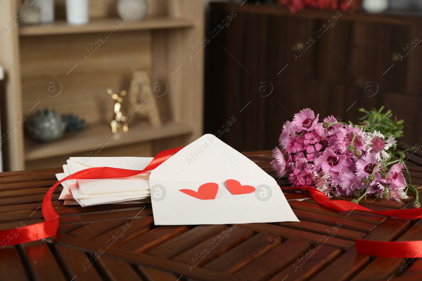 Love letters, red hearts, ribbon and flowers on wooden table indoors Photo of Love letters, red hearts, ribbon and flowers on wooden table indoors