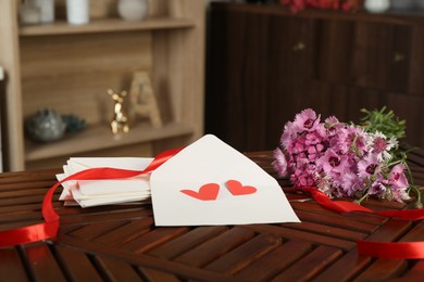 Photo of Love letters, red hearts, ribbon and flowers on wooden table indoors