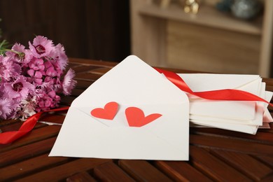 Photo of Love letters, red hearts, ribbon and flowers on wooden table indoors, closeup