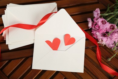 Photo of Love letters, red hearts, ribbon and flowers on wooden table indoors, flat lay