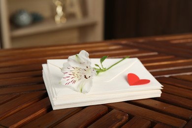 Photo of Stack of love letters, red heart and flower on wooden table indoors, closeup