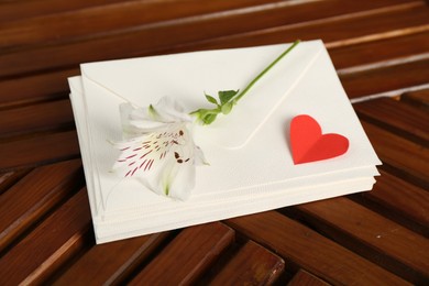 Photo of Stack of love letters, red heart and flower on wooden table, above view