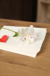 Photo of Stack of love letters, red heart and flower on wooden table indoors, closeup