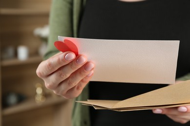 Photo of Woman with love letter, envelopes and red heart indoors, closeup