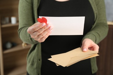 Photo of Woman with love letter, envelopes and red heart indoors, closeup