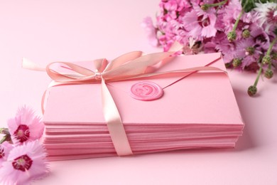 Photo of Stack of love letters and flowers on pink background, closeup