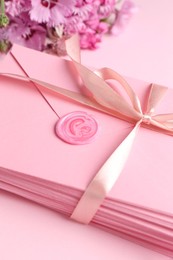 Photo of Stack of love letters and flowers on pink background, closeup