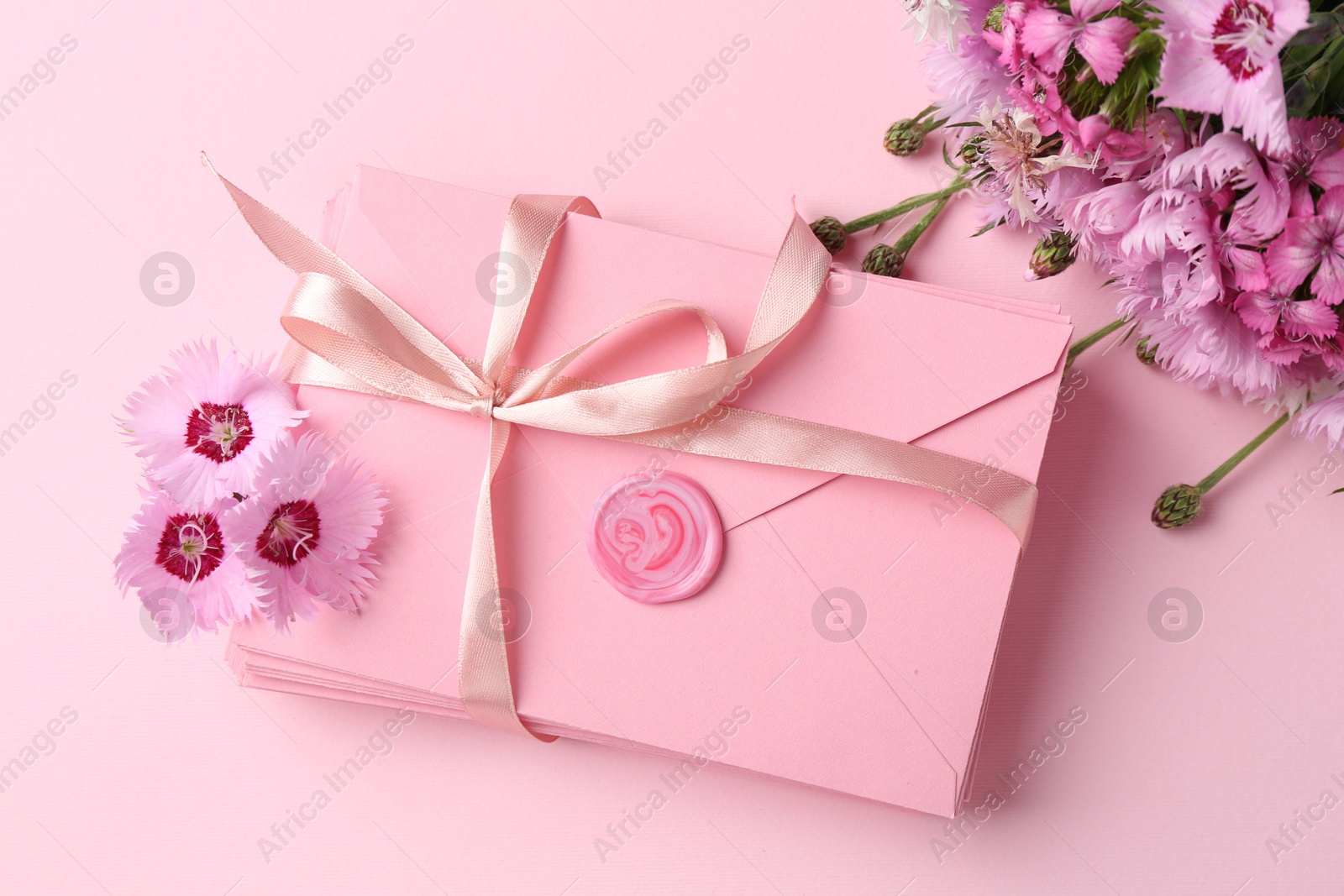 Stack of love letters and flowers on pink background, flat lay Photo of Stack of love letters and flowers on pink background, flat lay