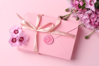 Photo of Stack of love letters and flowers on pink background, flat lay