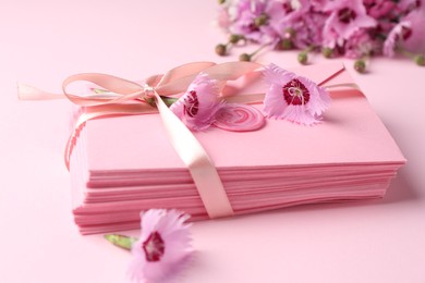 Photo of Stack of love letters and flowers on pink background, closeup