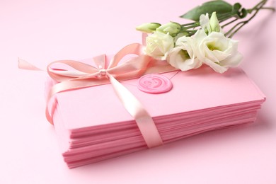 Photo of Stack of love letters and flowers on pink background, closeup