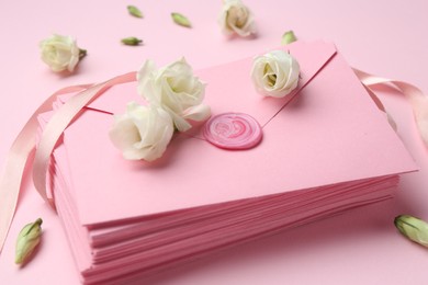 Photo of Stack of love letters and flowers on pink background, closeup