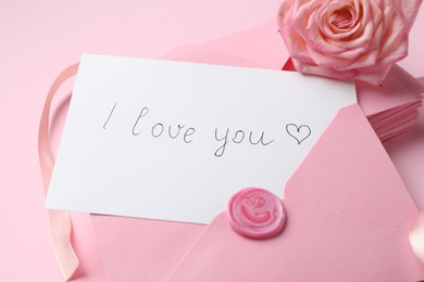 Photo of Stack of letters, card with phrase I Love You and rose flower on pink background, closeup