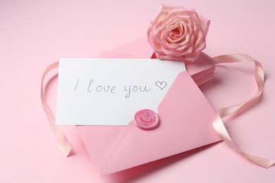 Photo of Stack of letters, card with phrase I Love You and rose flower on pink background, closeup