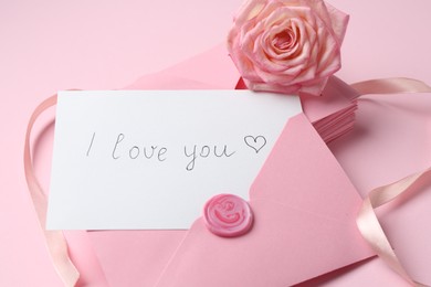 Photo of Stack of letters, card with phrase I Love You and rose flower on pink background, closeup