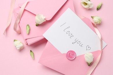 Photo of Stack of letters, card with phrase I Love You and flowers on pink background, flat lay