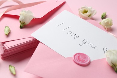 Photo of Stack of letters, card with phrase I Love You and flowers on pink background, closeup