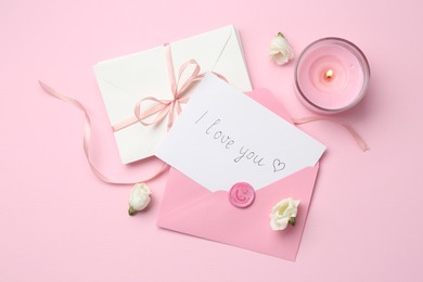 Photo of Stack of letters, card with phrase I Love You, burning candle and flowers on pink background, flat lay