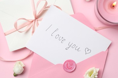 Photo of Stack of letters, card with phrase I Love You, burning candle and flowers on pink background, flat lay
