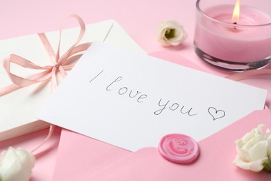Photo of Stack of letters, card with phrase I Love You, burning candle and flowers on pink background, closeup