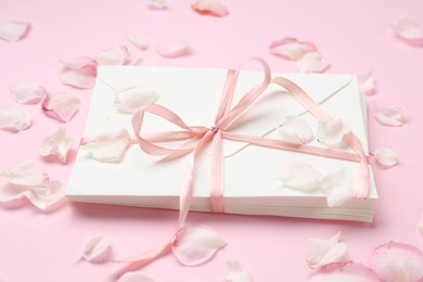Photo of Stack of love letters and petals on pink background, closeup