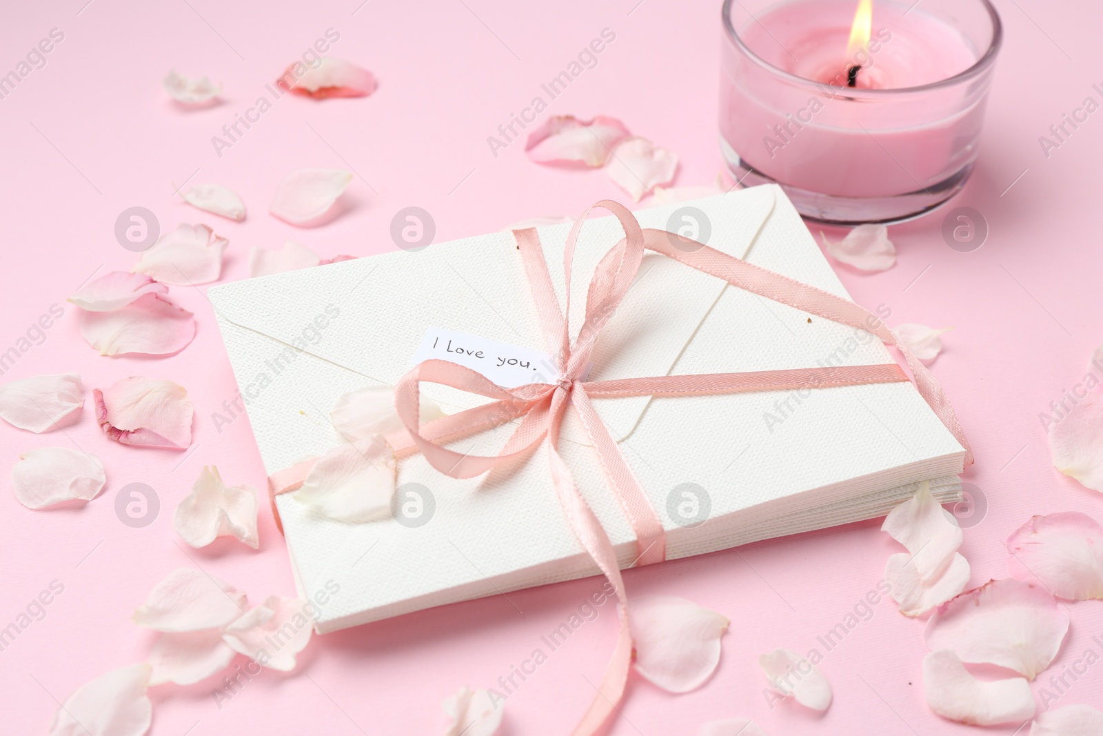 Stack of letters with phrase I Love You, burning candle and petals on pink background, closeup Photo of Stack of letters with phrase I Love You, burning candle and petals on pink background, closeup