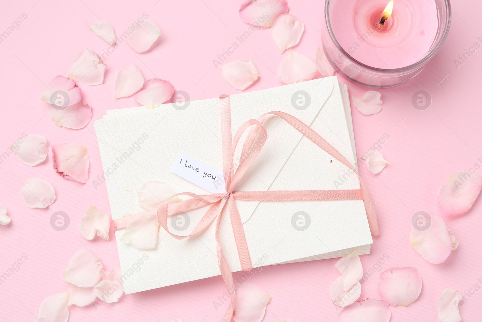 Stack of letters with phrase I Love You, burning candle and petals on pink background, flat lay Photo of Stack of letters with phrase I Love You, burning candle and petals on pink background, flat lay
