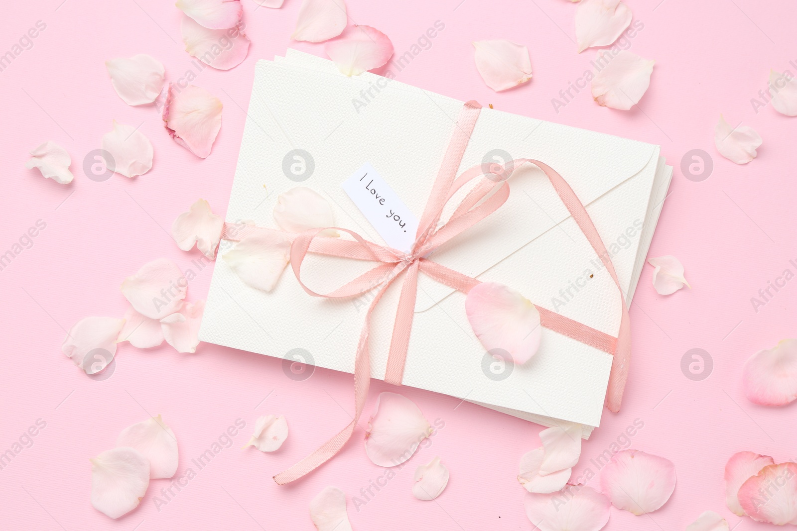 Stack of letters with phrase I Love You and petals on pink background, flat lay Photo of Stack of letters with phrase I Love You and petals on pink background, flat lay