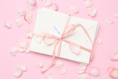 Photo of Stack of letters with phrase I Love You and petals on pink background, flat lay