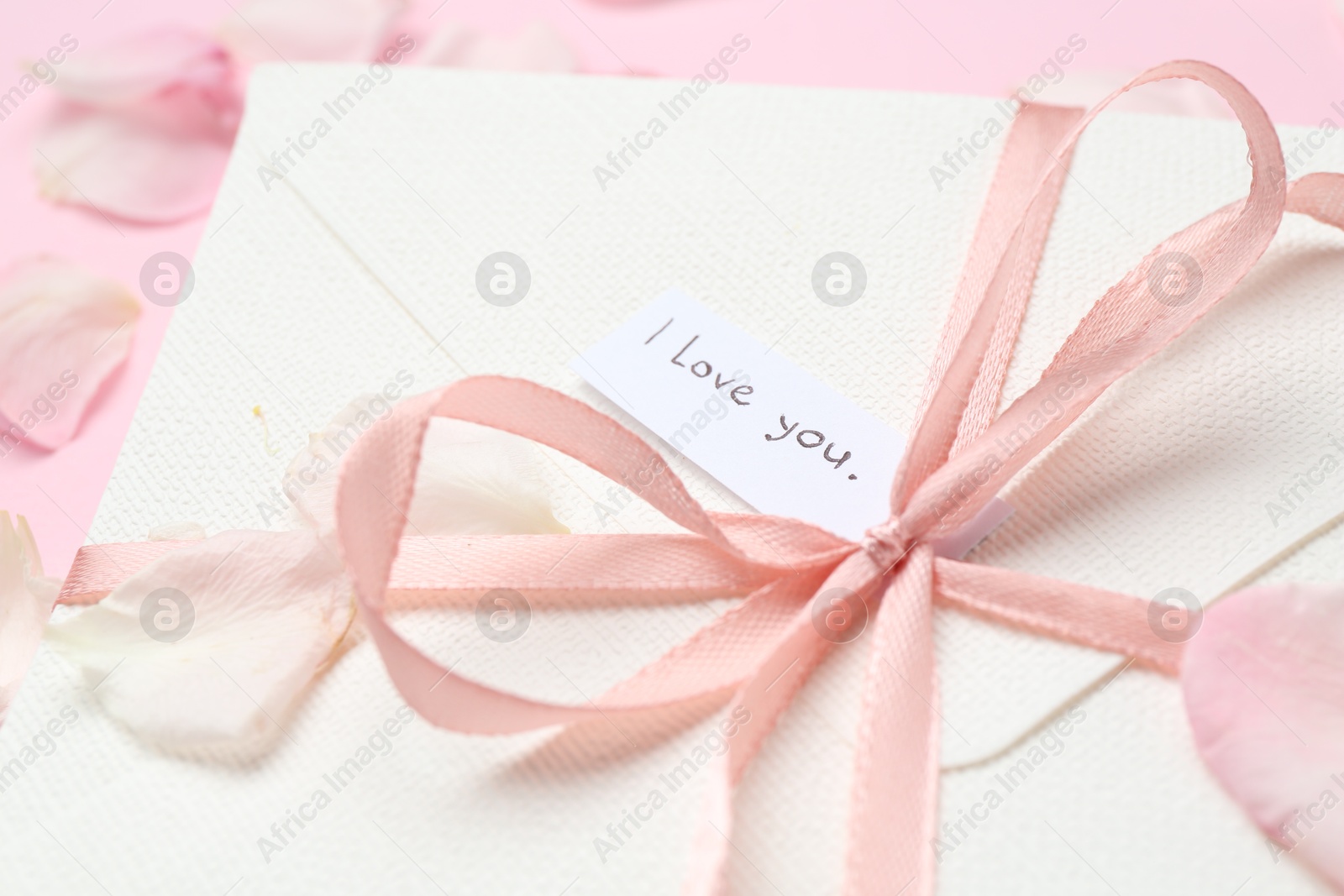 Envelope with phrase I Love You and petals on pink background, closeup Photo of Envelope with phrase I Love You and petals on pink background, closeup