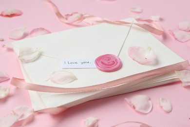 Photo of Stack of letters with phrase I Love You and petals on pink background, closeup
