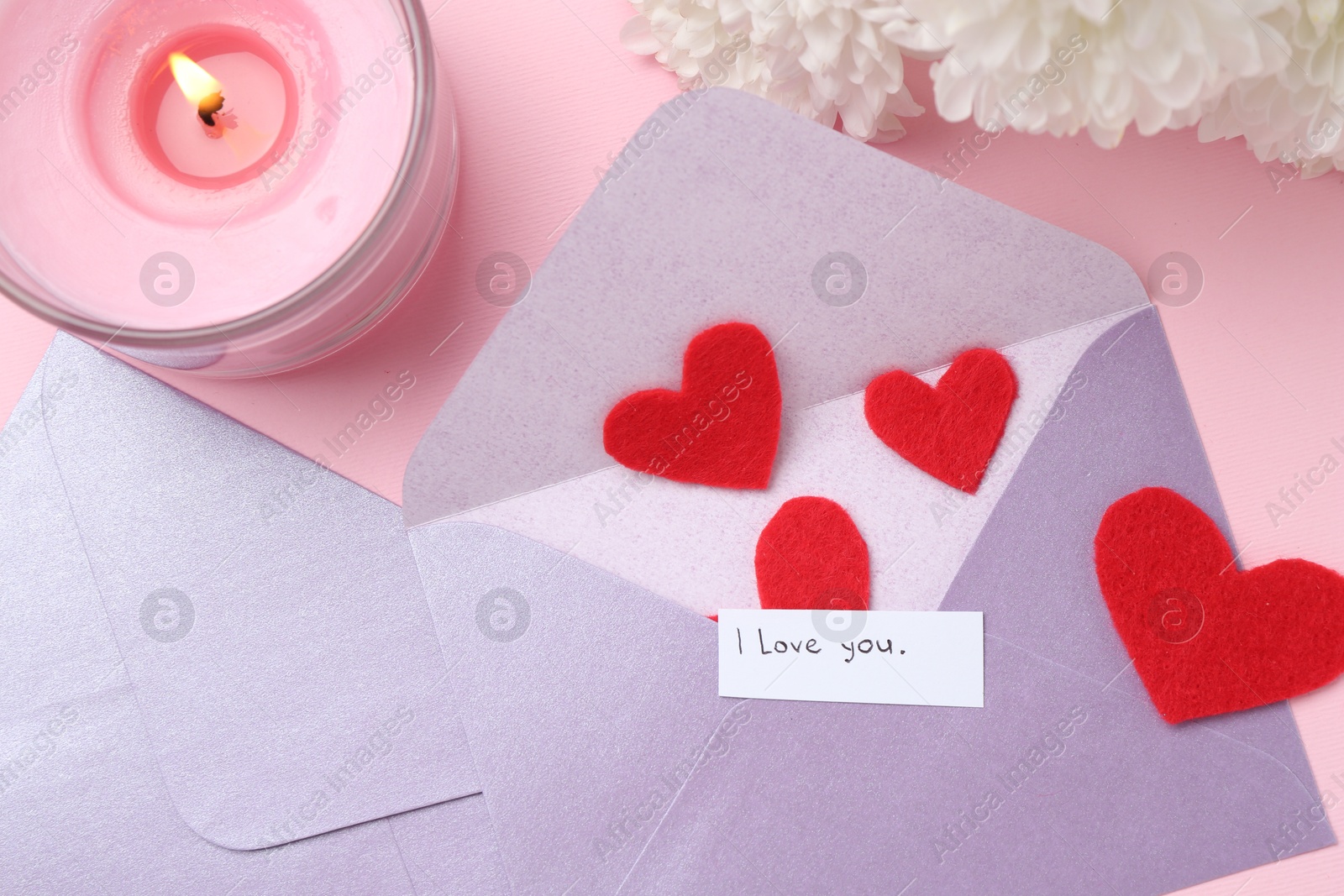 Envelopes with phrase I Love You, red hearts, burning candle and flowers on pink background, flat lay Photo of Envelopes with phrase I Love You, red hearts, burning candle and flowers on pink background, flat lay