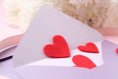 Photo of Love letter. Envelope, red hearts, ribbon and flowers on blurred background, closeup
