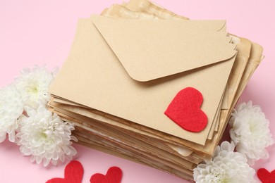 Photo of Stack of love letters, flowers and red hearts on pink background, above view