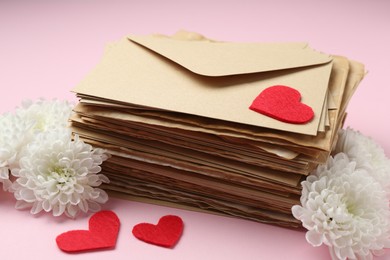 Photo of Stack of love letters, flowers and red hearts on pink background, closeup