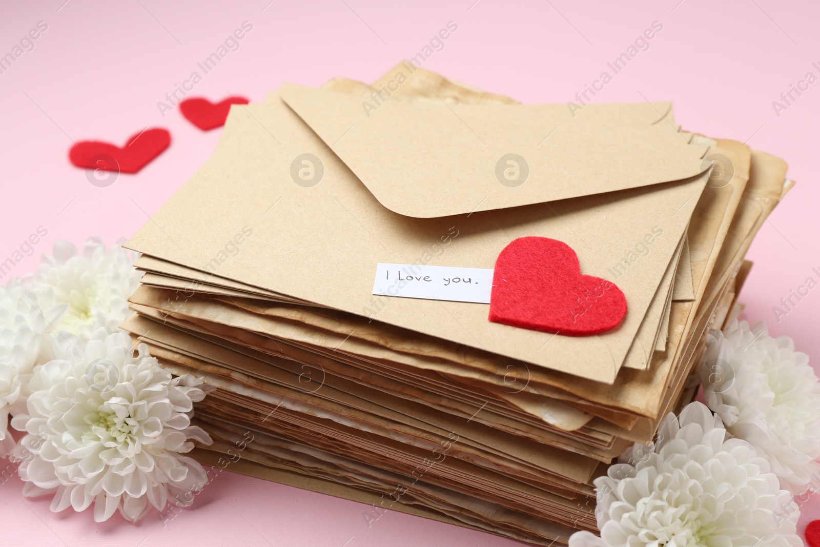 Stack of letters with phrase I Love You, flowers and red hearts on pink background, closeup Photo of Stack of letters with phrase I Love You, flowers and red hearts on pink background, closeup