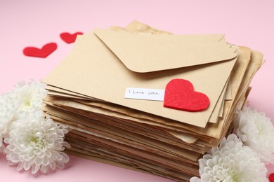 Photo of Stack of letters with phrase I Love You, flowers and red hearts on pink background, closeup
