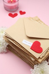 Photo of Stack of letters with phrase I Love You, flowers, burning candle and red hearts on pink background, above view