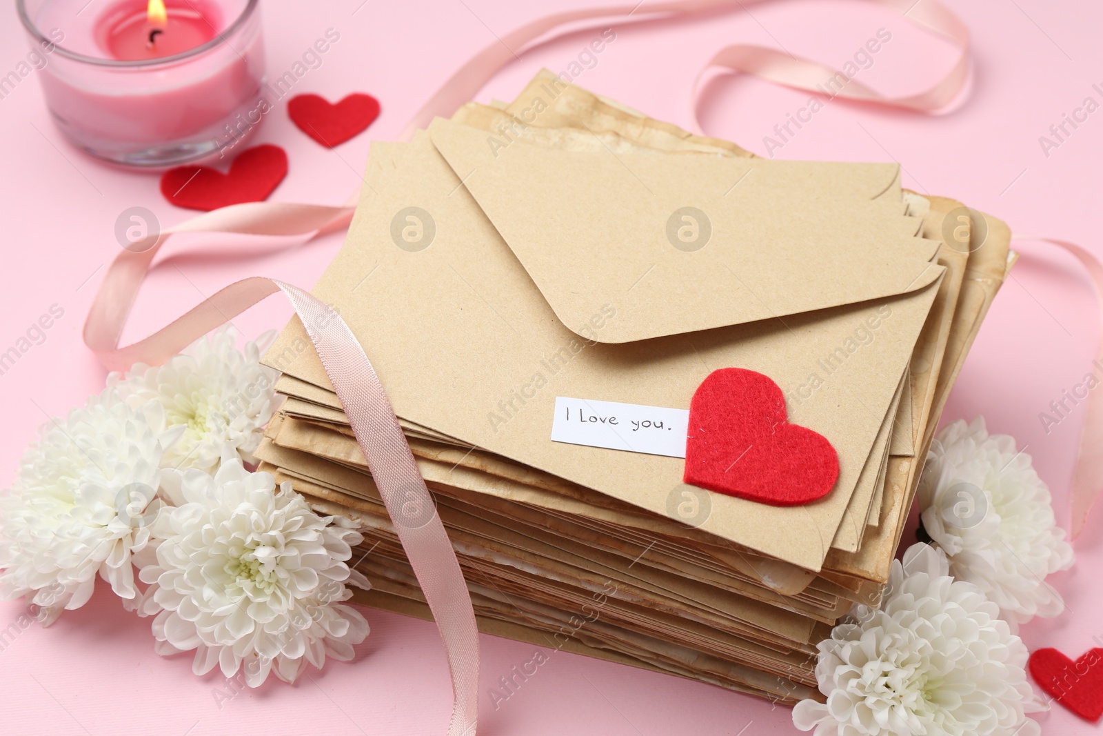 Stack of letters with phrase I Love You, flowers, burning candle and red hearts on pink background, above view Photo of Stack of letters with phrase I Love You, flowers, burning candle and red hearts on pink background, above view