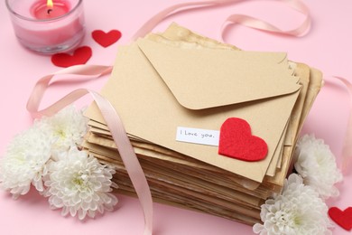 Photo of Stack of letters with phrase I Love You, flowers, burning candle and red hearts on pink background, above view