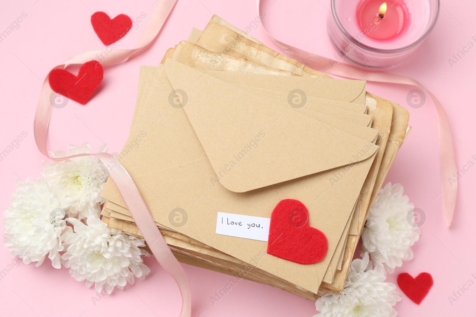 Stack of letters with phrase I Love You, flowers, burning candle and red hearts on pink background, flat lay Photo of Stack of letters with phrase I Love You, flowers, burning candle and red hearts on pink background, flat lay