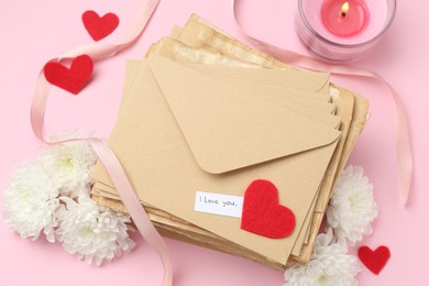 Photo of Stack of letters with phrase I Love You, flowers, burning candle and red hearts on pink background, flat lay