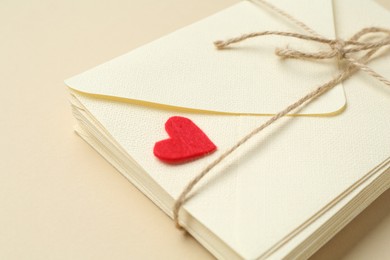 Photo of Stack of love letters and red heart on beige background, closeup