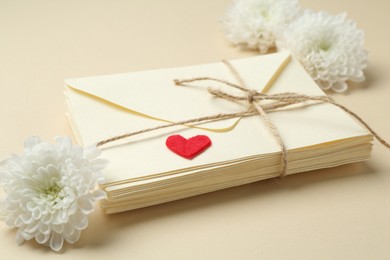 Photo of Stack of love letters, flowers and red heart on beige background, closeup