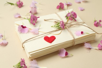 Photo of Stack of love letters, flowers and red heart on beige background, closeup