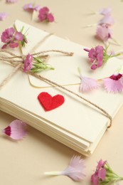 Photo of Stack of love letters, flowers and red heart on beige background, closeup