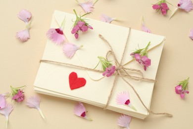 Photo of Stack of love letters, flowers and red heart on beige background, flat lay