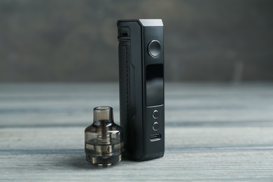 Photo of Electronic smoking device and cartridge on wooden table against grey background, closeup