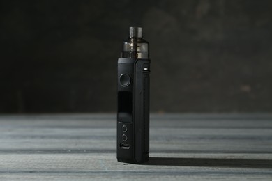 Photo of One electronic smoking device on grey wooden table against dark background, closeup