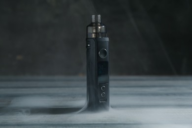 Photo of One electronic smoking device in smoke on grey wooden table against dark background, closeup